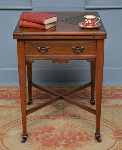 fig 1. An antique mahogany envelope card table featuring four triangular top flaps, a single drawer with brass drop handles, and tapered legs joined by an X-shaped stretcher.