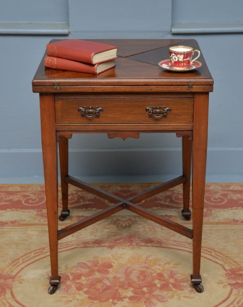 fig 3. An antique mahogany envelope card table featuring four triangular top flaps, a single drawer with brass drop handles, and tapered legs joined by an X-shaped stretcher.