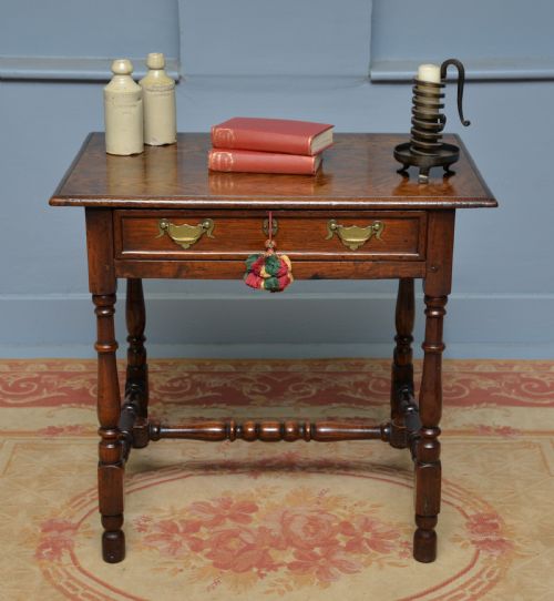 fig 1. An early 18th-century dark oak side table featuring a rectangular top, single frieze drawer with brass handles, turned legs, and a stretcher base.
