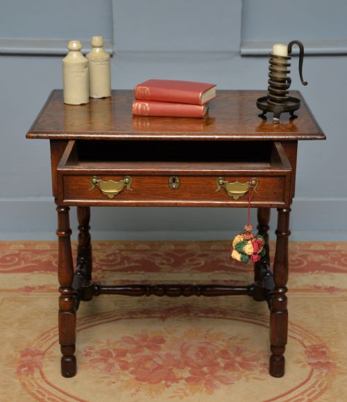 fig 2. An early 18th-century dark oak side table featuring a rectangular top, single frieze drawer with brass handles, turned legs, and a stretcher base.