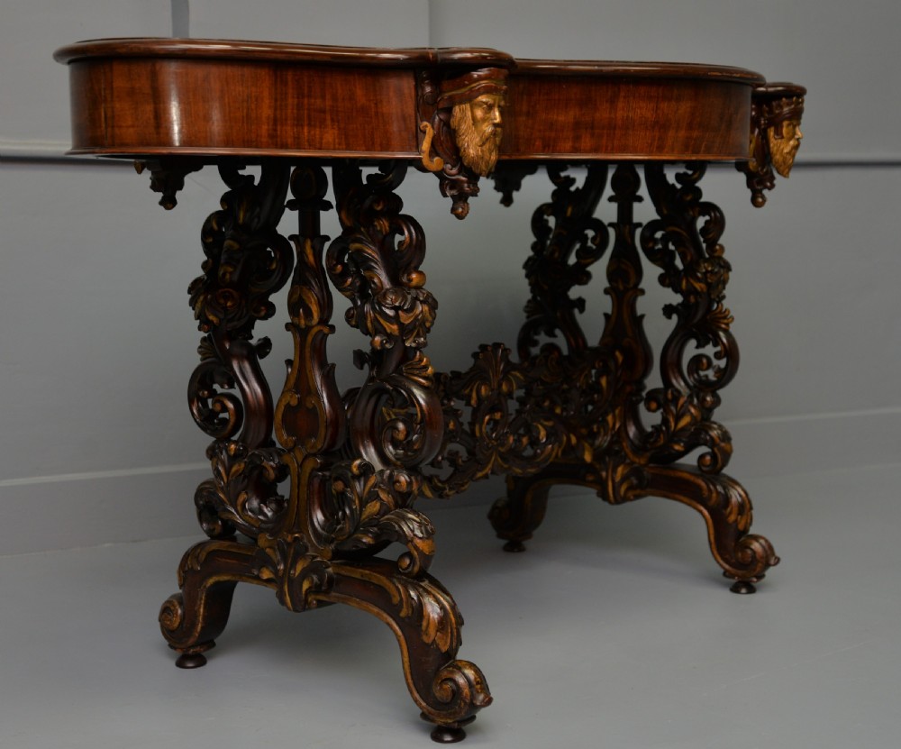 A 19th-century dark carved mahogany centre table featuring a shaped top, parcel-gilt mask corner details, and intricate openwork scroll legs. View V