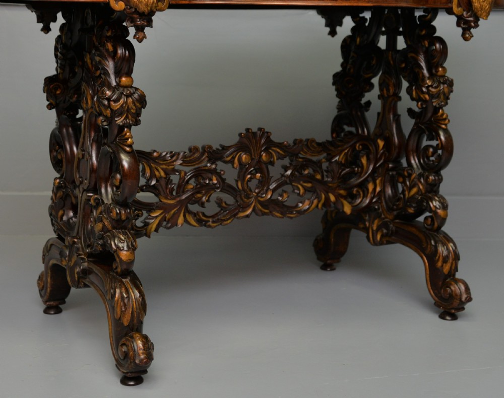 A 19th-century dark carved mahogany centre table featuring a shaped top, parcel-gilt mask corner details, and intricate openwork scroll legs. View VI
