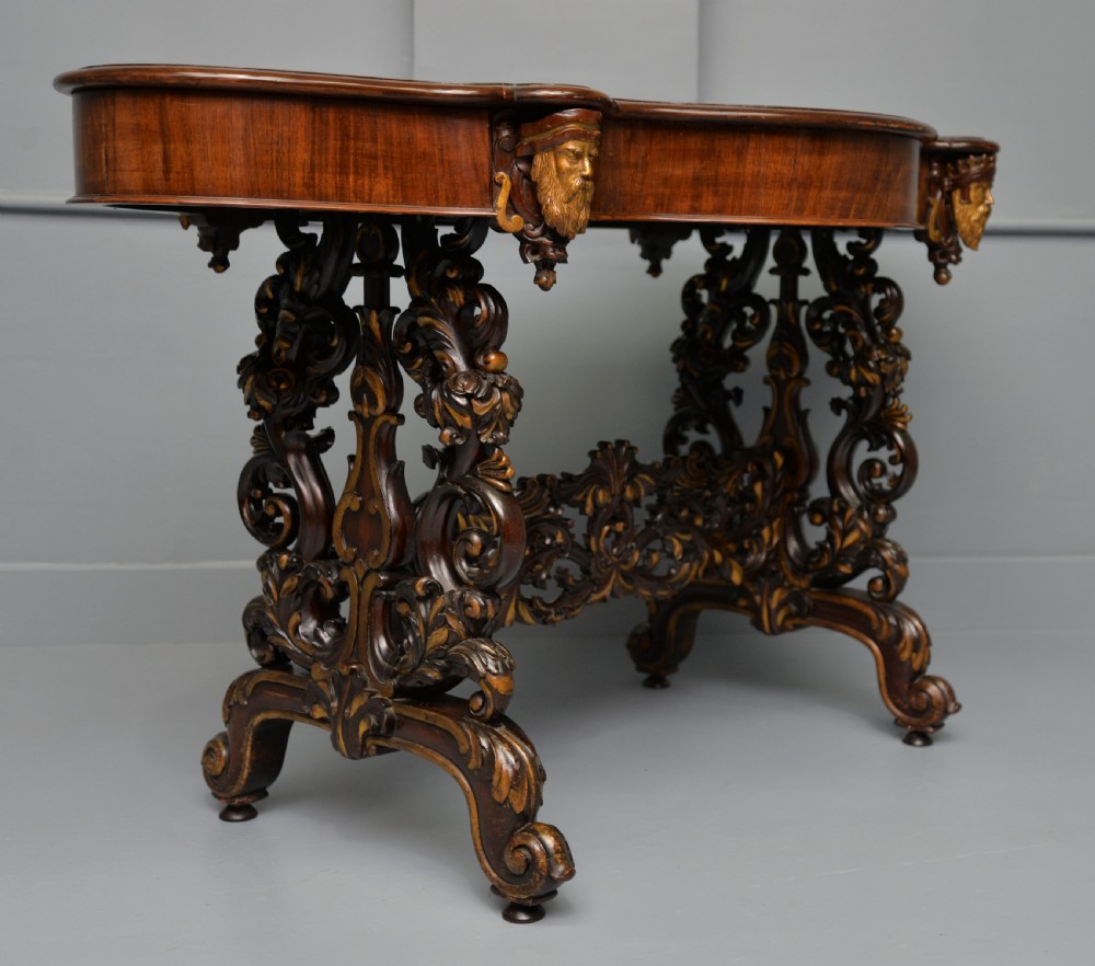 A 19th-century dark carved mahogany centre table featuring a shaped top, parcel-gilt mask corner details, and intricate openwork scroll legs. View VIII
