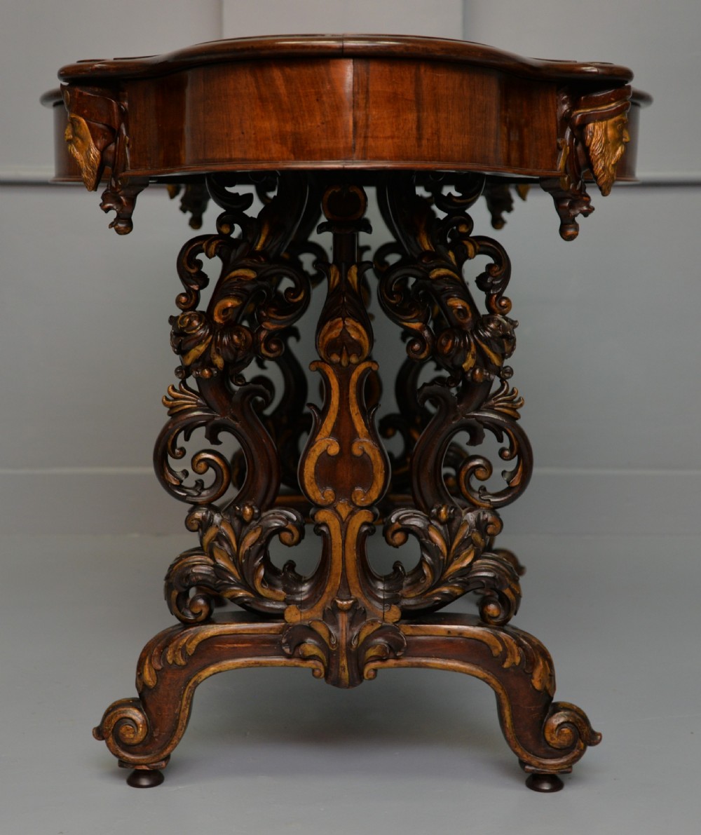 A 19th-century dark carved mahogany centre table featuring a shaped top, parcel-gilt mask corner details, and intricate openwork scroll legs. View IX