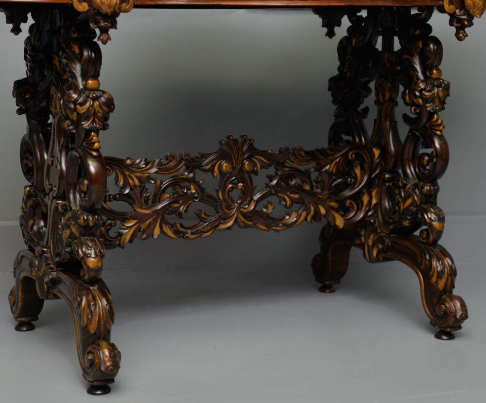 A 19th-century dark carved mahogany centre table featuring a shaped top, parcel-gilt mask corner details, and intricate openwork scroll legs. View X