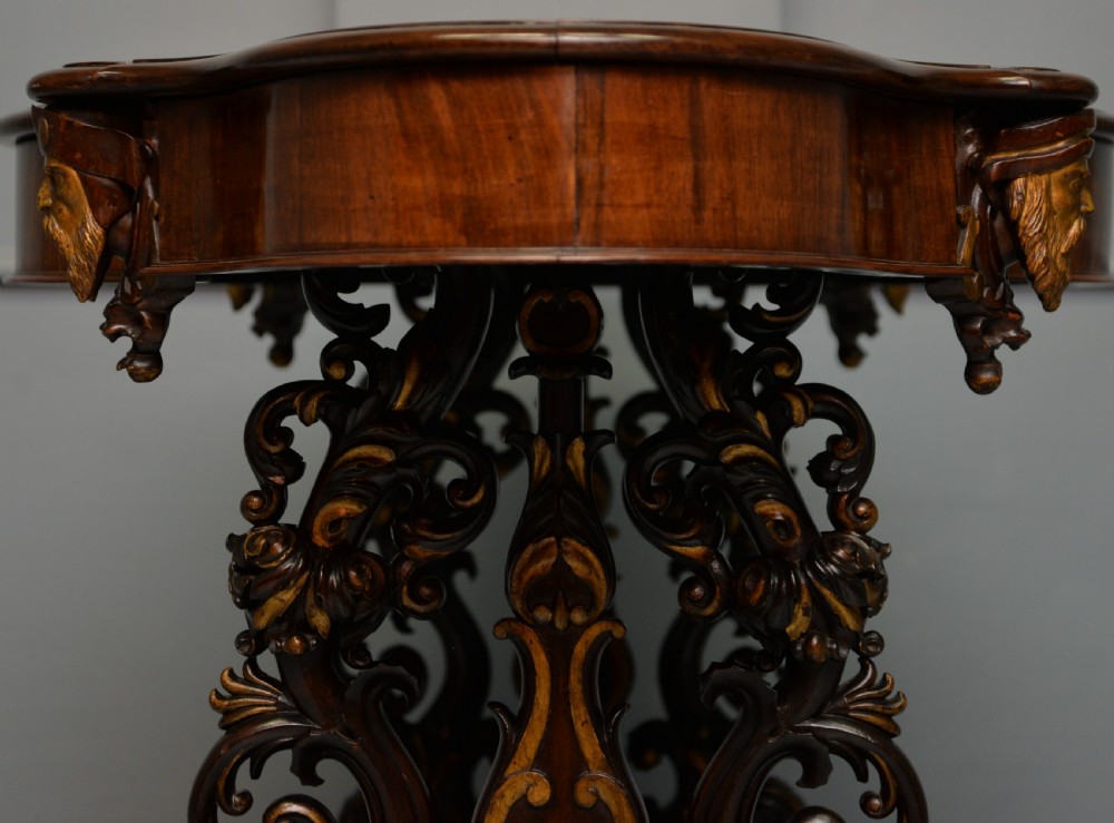 A 19th-century dark carved mahogany centre table featuring a shaped top, parcel-gilt mask corner details, and intricate openwork scroll legs. View XII