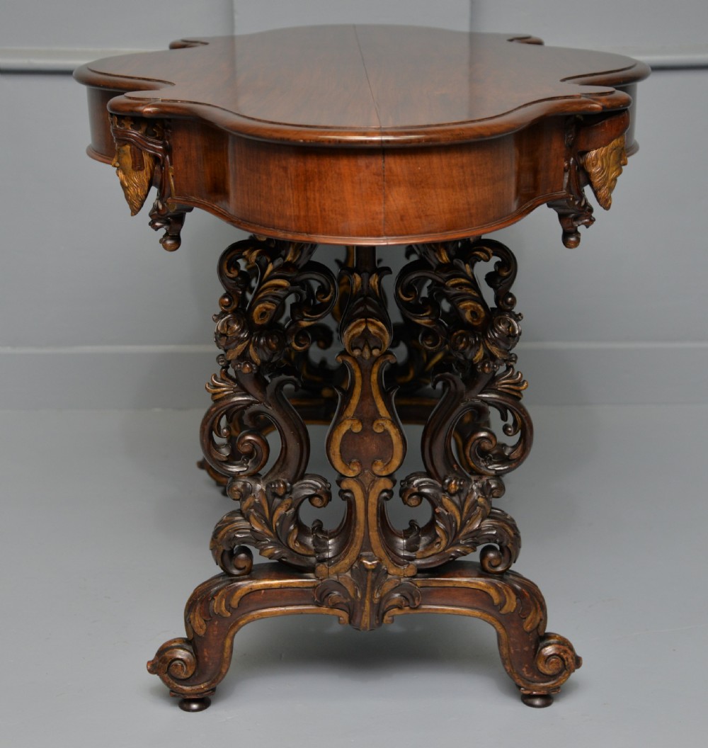 A 19th-century dark carved mahogany centre table featuring a shaped top, parcel-gilt mask corner details, and intricate openwork scroll legs. View XVIII