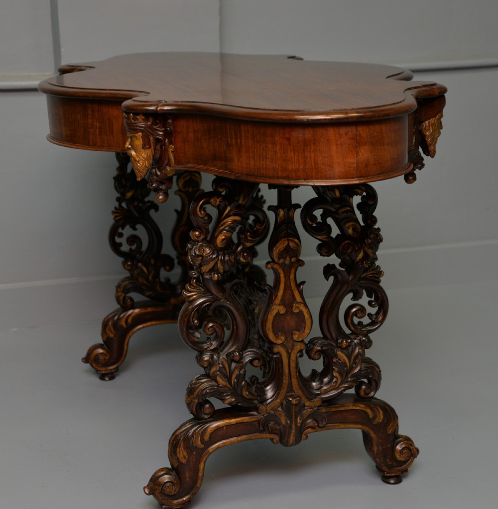 A 19th-century dark carved mahogany centre table featuring a shaped top, parcel-gilt mask corner details, and intricate openwork scroll legs. View XX