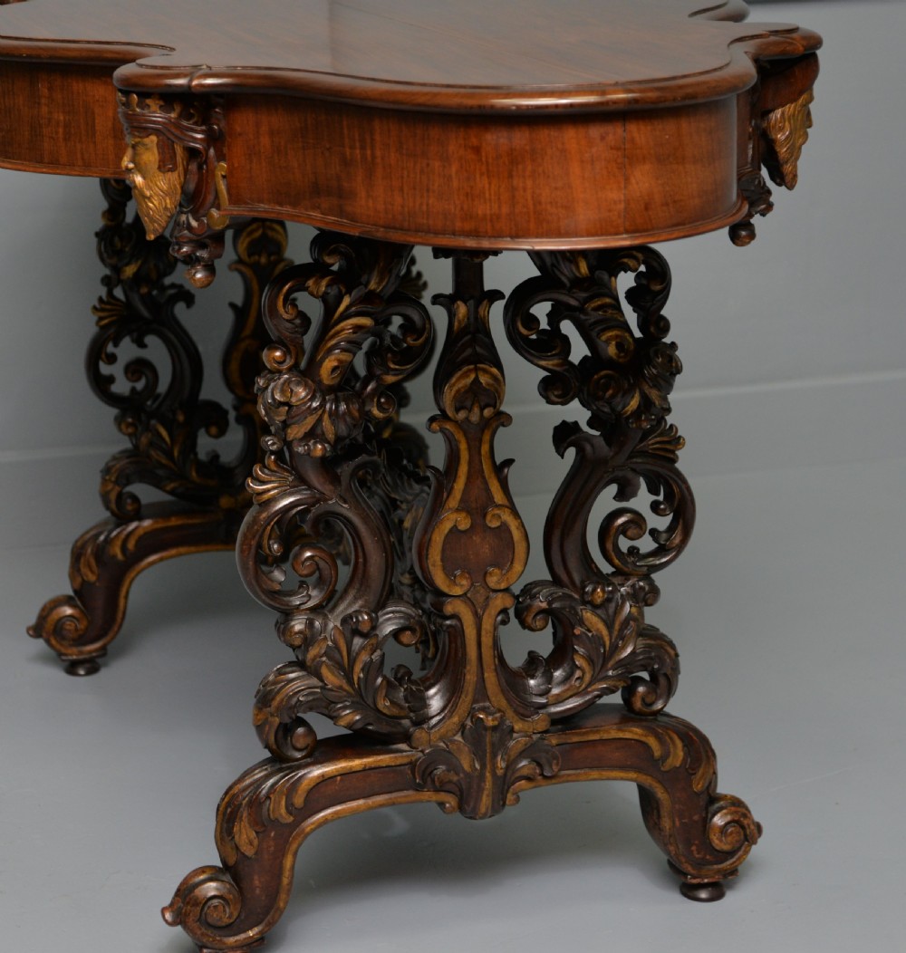 A 19th-century dark carved mahogany centre table featuring a shaped top, parcel-gilt mask corner details, and intricate openwork scroll legs. View XXI