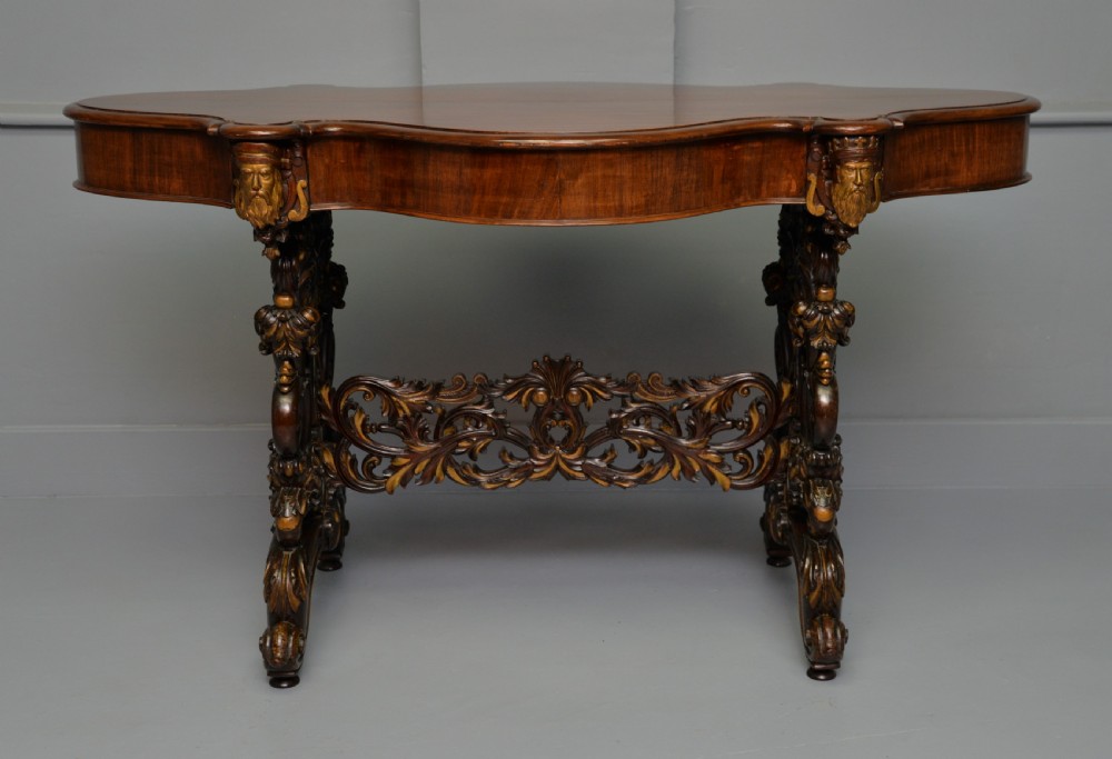 A 19th-century dark carved mahogany centre table featuring a shaped top, parcel-gilt mask corner details, and intricate openwork scroll legs. View XXII