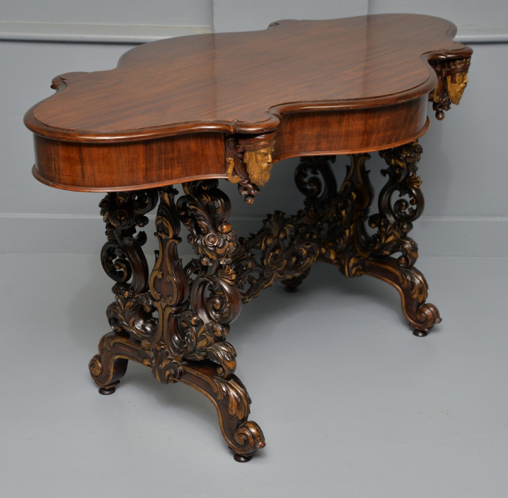 A 19th-century dark carved mahogany centre table featuring a shaped top, parcel-gilt mask corner details, and intricate openwork scroll legs. View XXIII