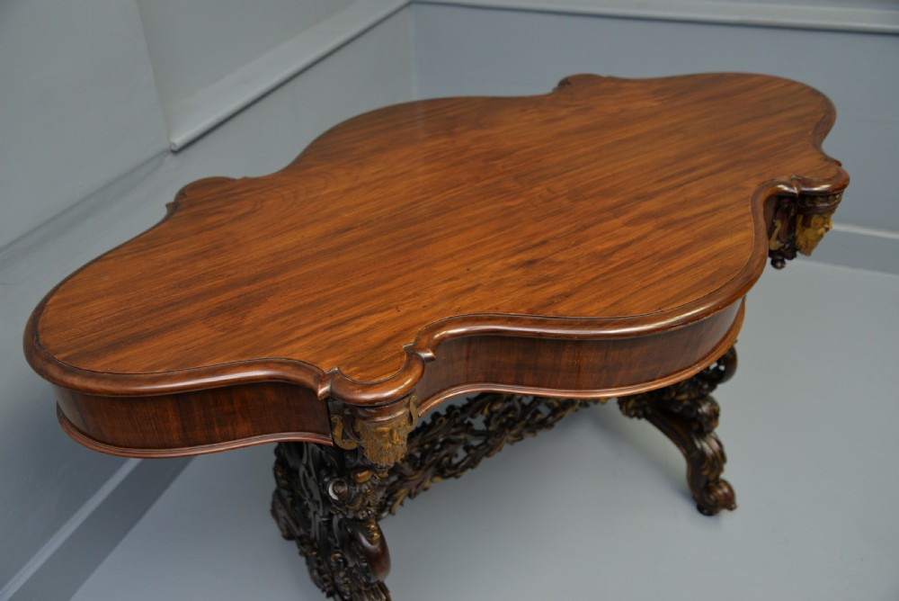A 19th-century dark carved mahogany centre table featuring a shaped top, parcel-gilt mask corner details, and intricate openwork scroll legs. View XXIV