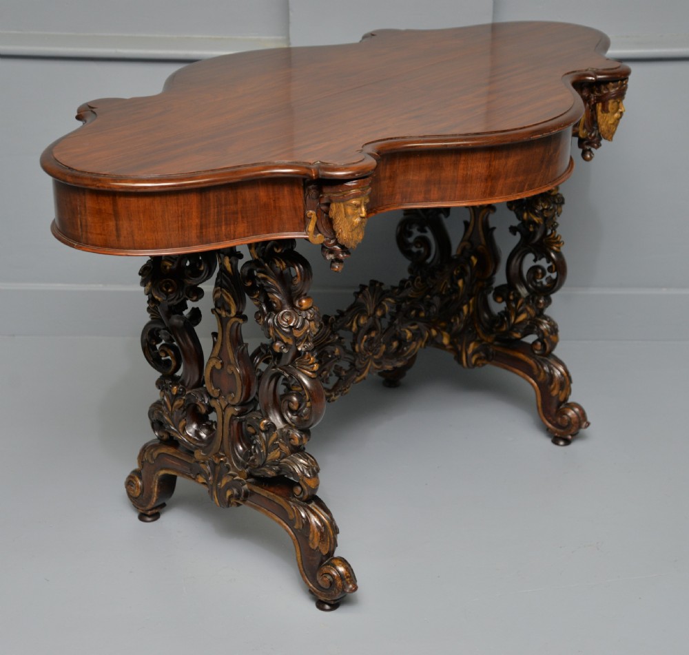 A 19th-century dark carved mahogany centre table featuring a shaped top, parcel-gilt mask corner details, and intricate openwork scroll legs. View XXV