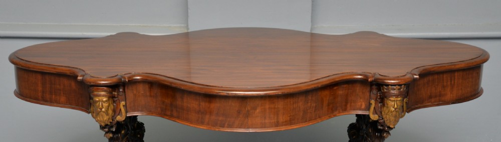 A 19th-century dark carved mahogany centre table featuring a shaped top, parcel-gilt mask corner details, and intricate openwork scroll legs. View XXVIII