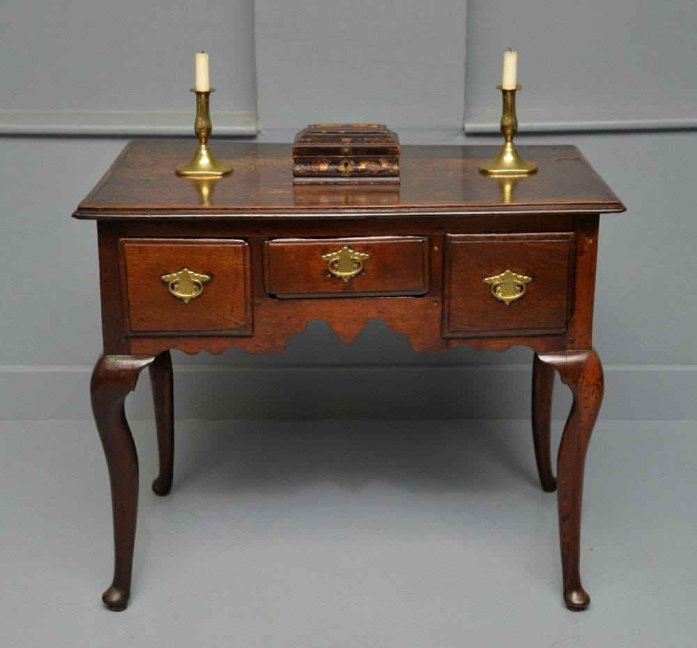 An early eighteenth-century oak lowboy featuring three drawers with brass handles, a scalloped apron, and four cabriole legs with pad feet.