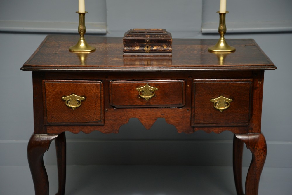 An early eighteenth-century oak lowboy featuring three drawers with brass handles, a scalloped apron, and four cabriole legs with pad feet. View II