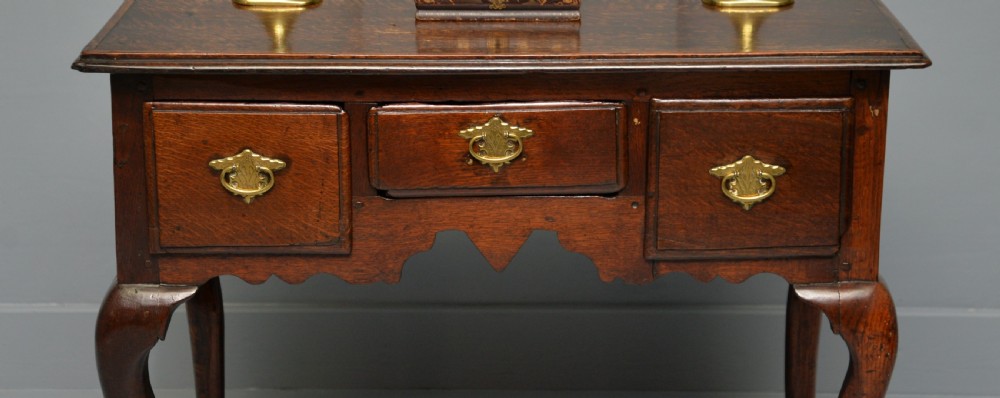 An early eighteenth-century oak lowboy featuring three drawers with brass handles, a scalloped apron, and four cabriole legs with pad feet. View III