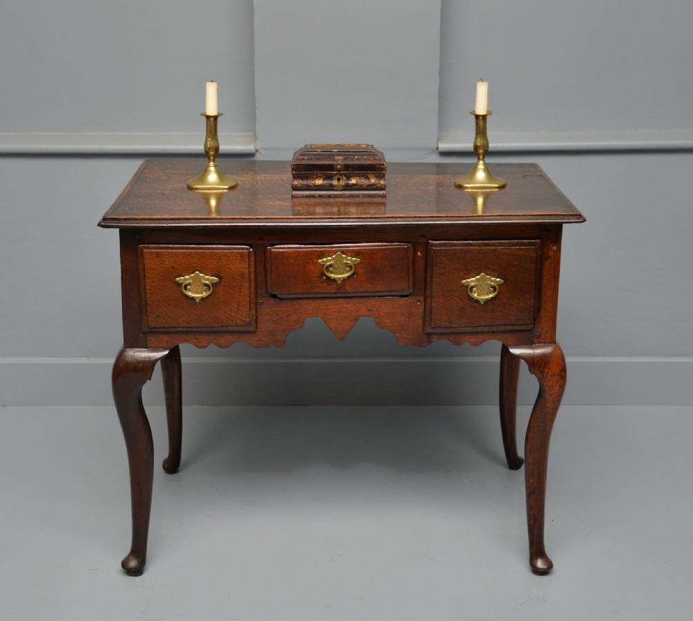 An early eighteenth-century oak lowboy featuring three drawers with brass handles, a scalloped apron, and four cabriole legs with pad feet. View V