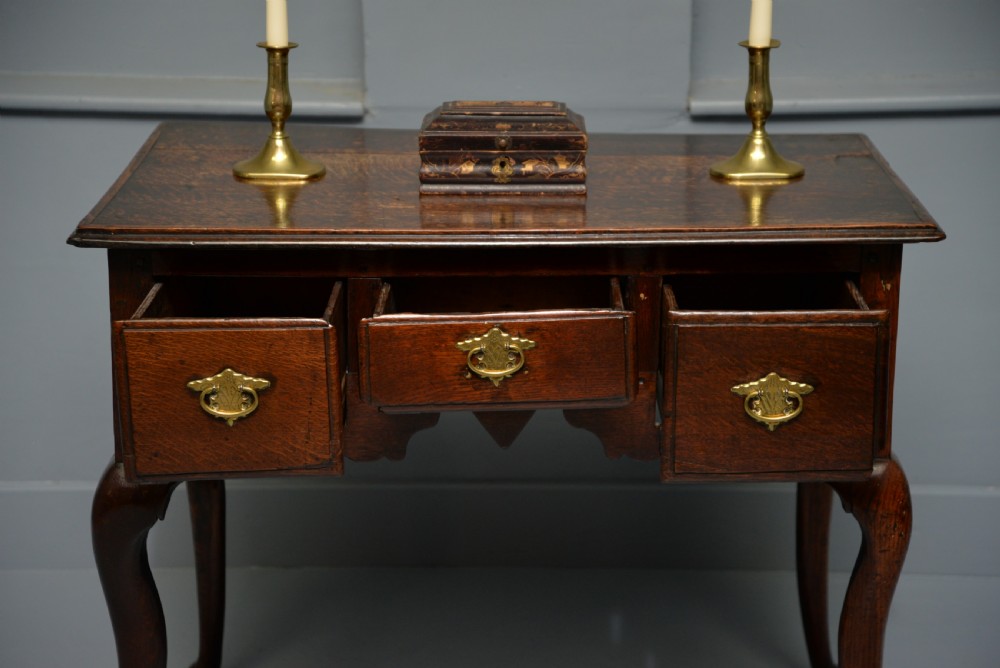 An early eighteenth-century oak lowboy featuring three drawers with brass handles, a scalloped apron, and four cabriole legs with pad feet. View VI