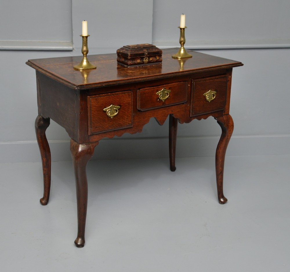 An early eighteenth-century oak lowboy featuring three drawers with brass handles, a scalloped apron, and four cabriole legs with pad feet. View VII