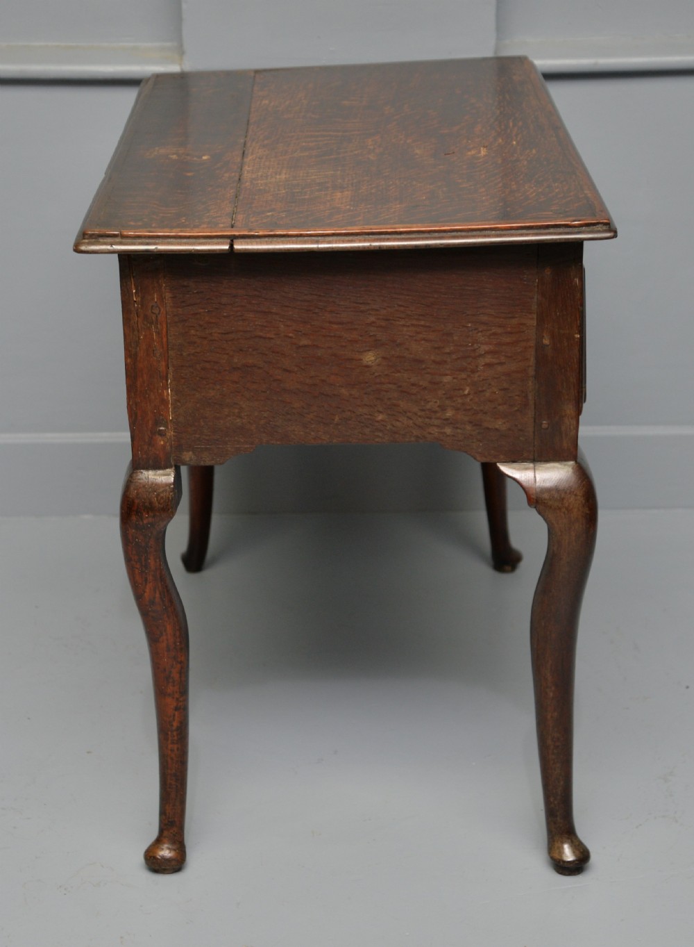An early eighteenth-century oak lowboy featuring three drawers with brass handles, a scalloped apron, and four cabriole legs with pad feet. View VIII
