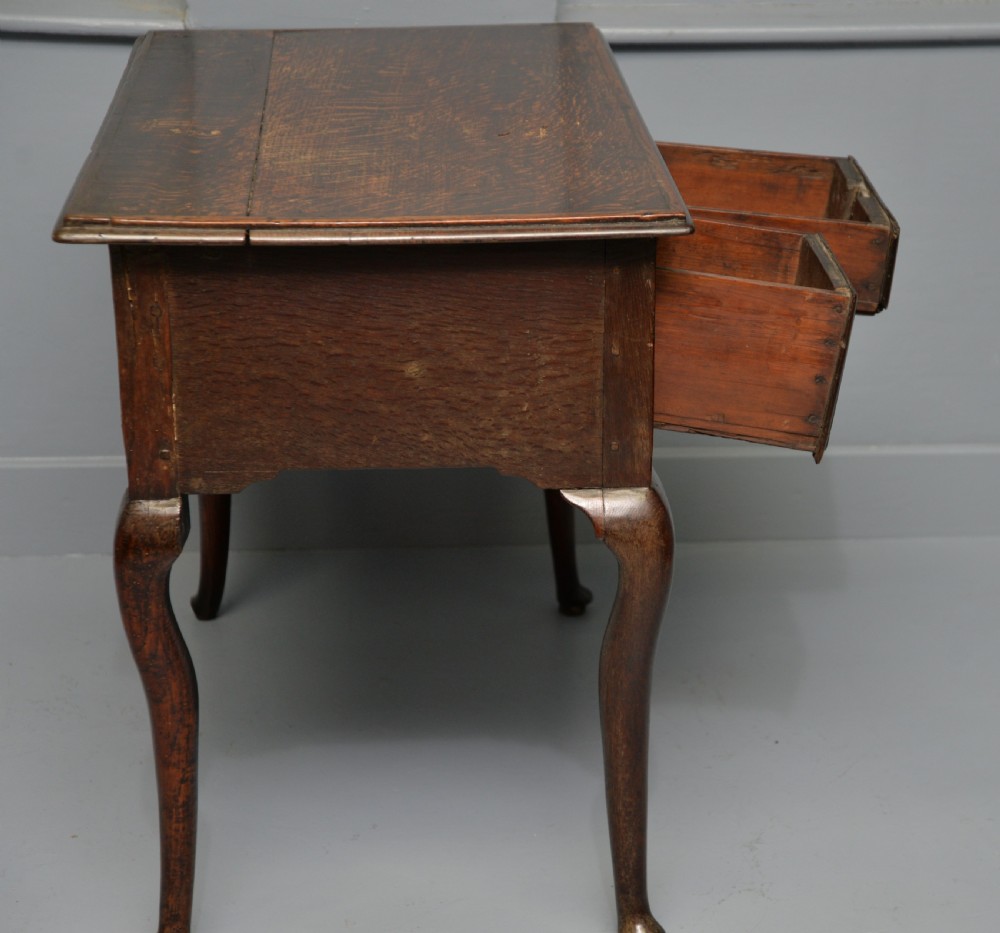 An early eighteenth-century oak lowboy featuring three drawers with brass handles, a scalloped apron, and four cabriole legs with pad feet. View IX