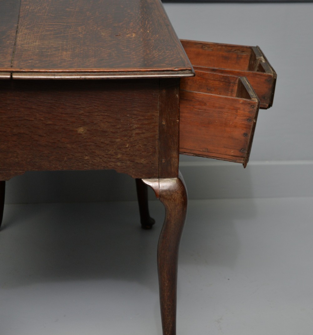 An early eighteenth-century oak lowboy featuring three drawers with brass handles, a scalloped apron, and four cabriole legs with pad feet. View X