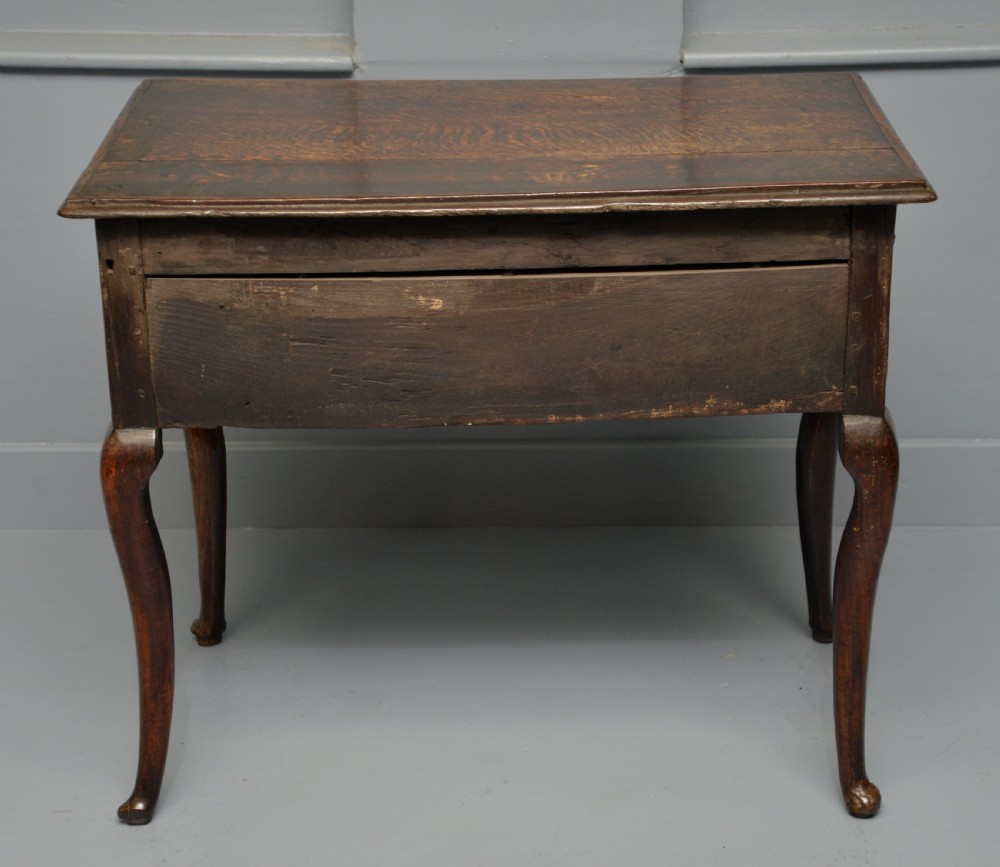 An early eighteenth-century oak lowboy featuring three drawers with brass handles, a scalloped apron, and four cabriole legs with pad feet. View XI