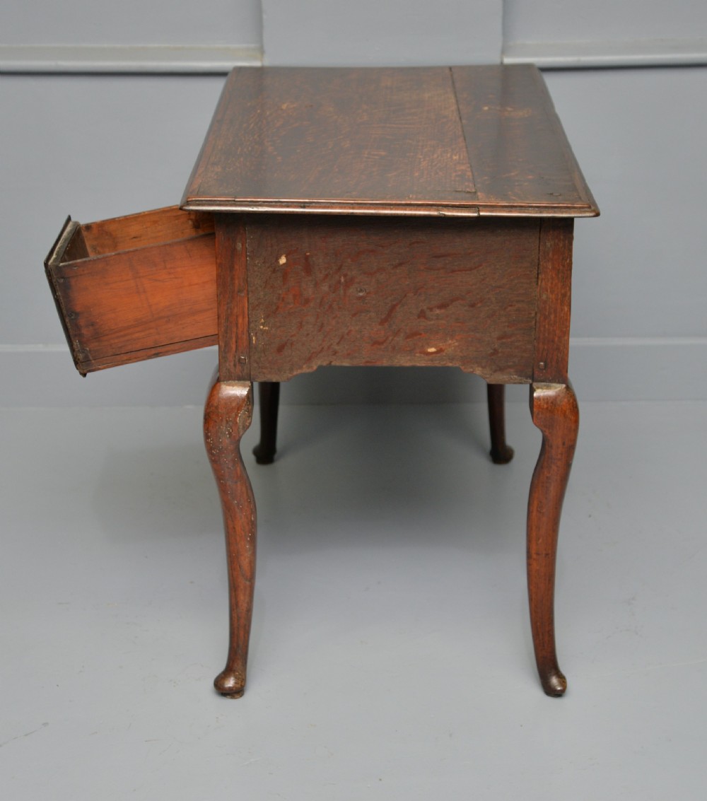 An early eighteenth-century oak lowboy featuring three drawers with brass handles, a scalloped apron, and four cabriole legs with pad feet. View XIV