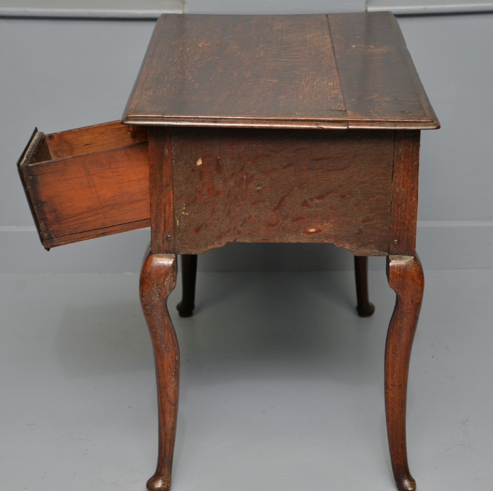 An early eighteenth-century oak lowboy featuring three drawers with brass handles, a scalloped apron, and four cabriole legs with pad feet. View XV
