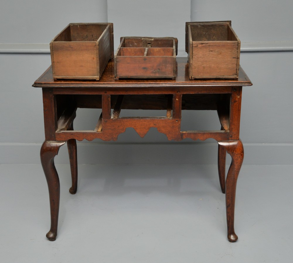 An early eighteenth-century oak lowboy featuring three drawers with brass handles, a scalloped apron, and four cabriole legs with pad feet. View XVI