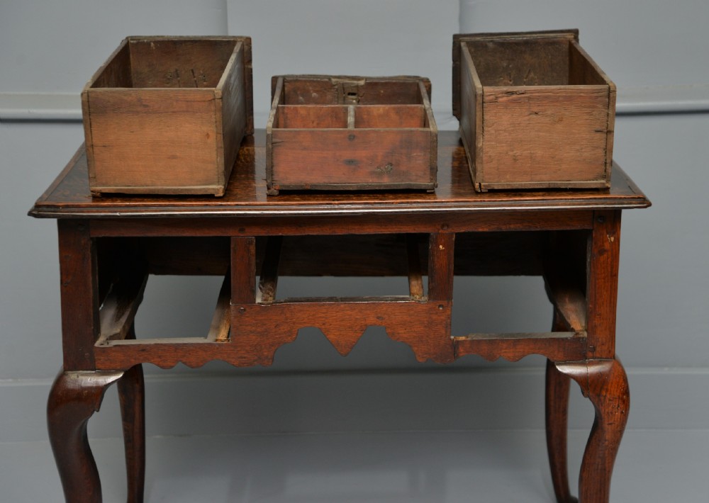 An early eighteenth-century oak lowboy featuring three drawers with brass handles, a scalloped apron, and four cabriole legs with pad feet. View XVIII