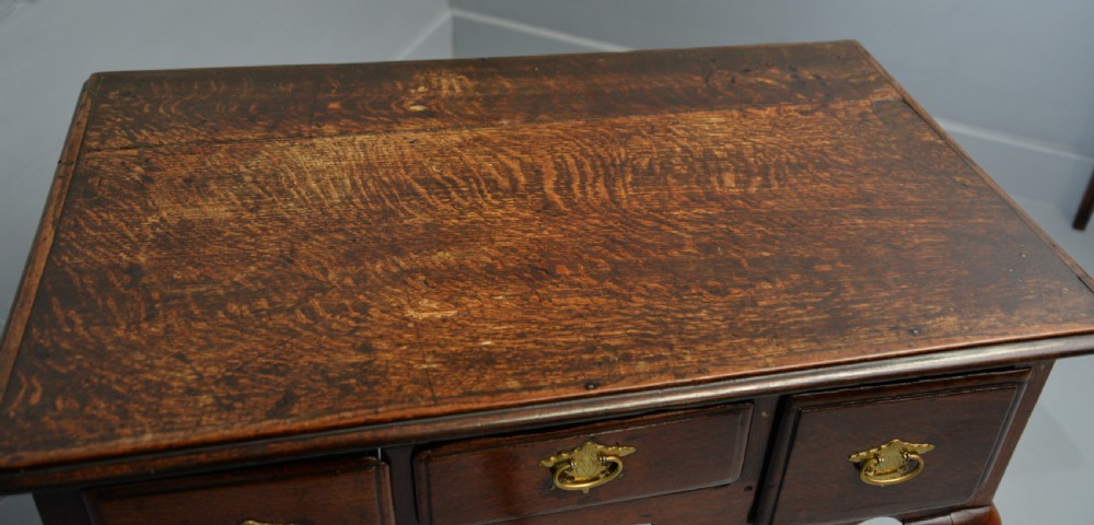 An early eighteenth-century oak lowboy featuring three drawers with brass handles, a scalloped apron, and four cabriole legs with pad feet. View XXI
