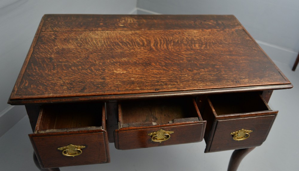 An early eighteenth-century oak lowboy featuring three drawers with brass handles, a scalloped apron, and four cabriole legs with pad feet. View XXII
