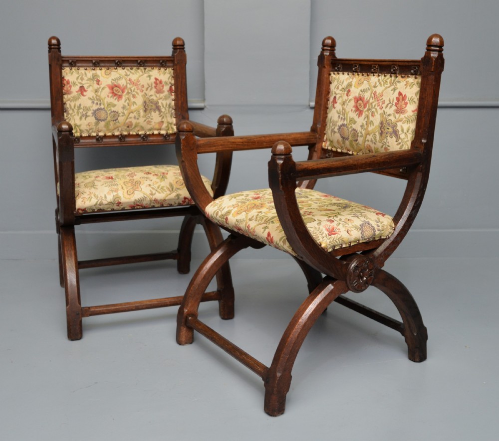 A pair of Victorian Gothic Revival dark oak X-frame armchairs featuring carved rosettes and floral tapestry upholstered seats and backrests with brass tack trimming. View III