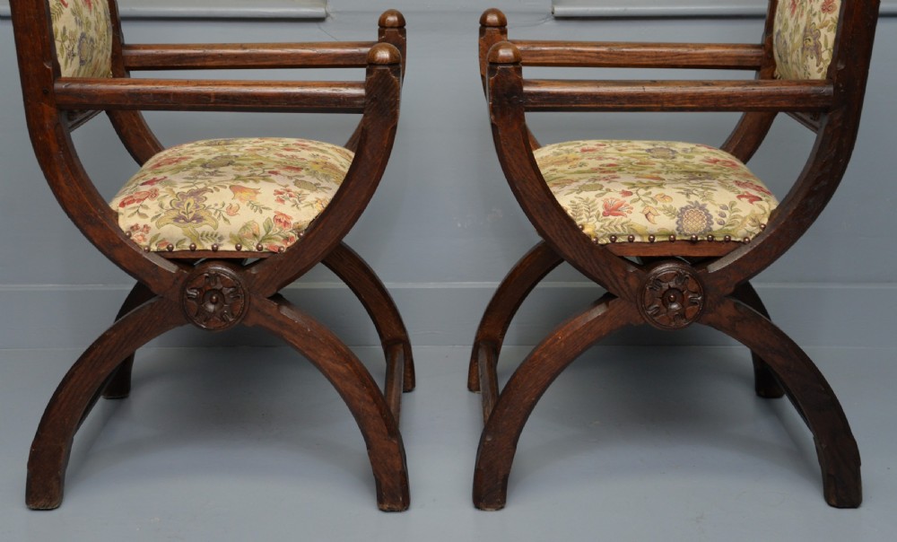 A pair of Victorian Gothic Revival dark oak X-frame armchairs featuring carved rosettes and floral tapestry upholstered seats and backrests with brass tack trimming. View VIII