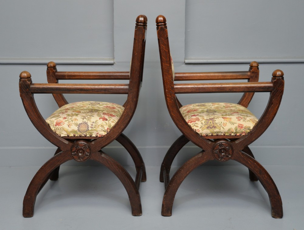 A pair of Victorian Gothic Revival dark oak X-frame armchairs featuring carved rosettes and floral tapestry upholstered seats and backrests with brass tack trimming. View XI