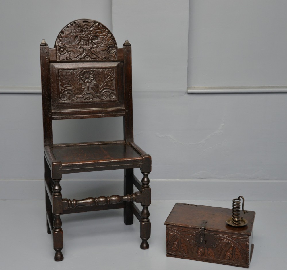 A dark carved oak 17th-century style backstool chair featuring an arched carved cresting rail, a carved floral back panel, turned front legs, and stretchers. View II