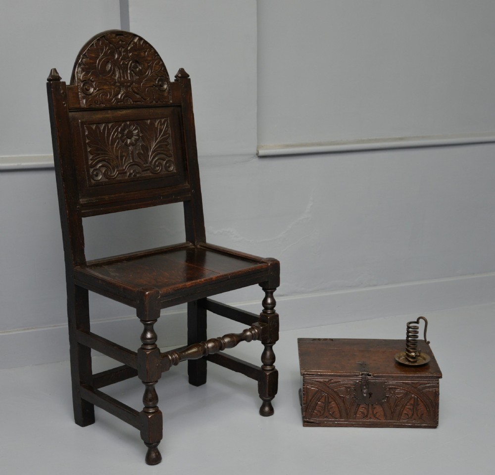 A dark carved oak 17th-century style backstool chair featuring an arched carved cresting rail, a carved floral back panel, turned front legs, and stretchers. View III