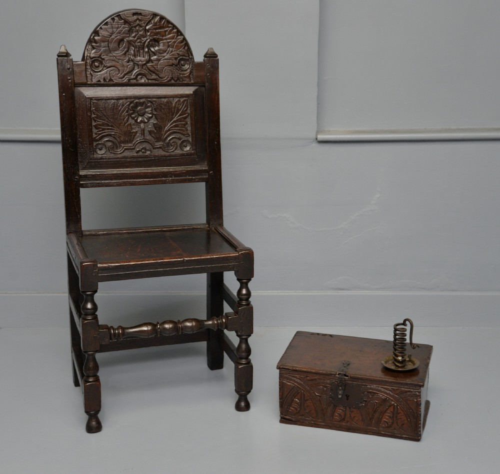 A dark carved oak 17th-century style backstool chair featuring an arched carved cresting rail, a carved floral back panel, turned front legs, and stretchers. View X