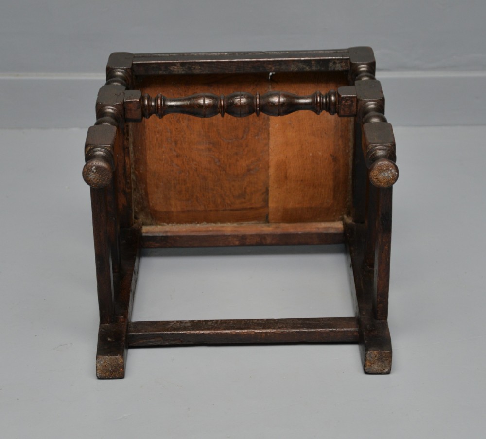 A dark carved oak 17th-century style backstool chair featuring an arched carved cresting rail, a carved floral back panel, turned front legs, and stretchers. View XVII