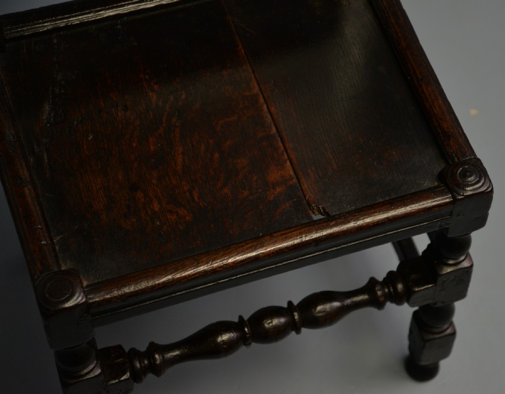 A dark carved oak 17th-century style backstool chair featuring an arched carved cresting rail, a carved floral back panel, turned front legs, and stretchers. View XVIII