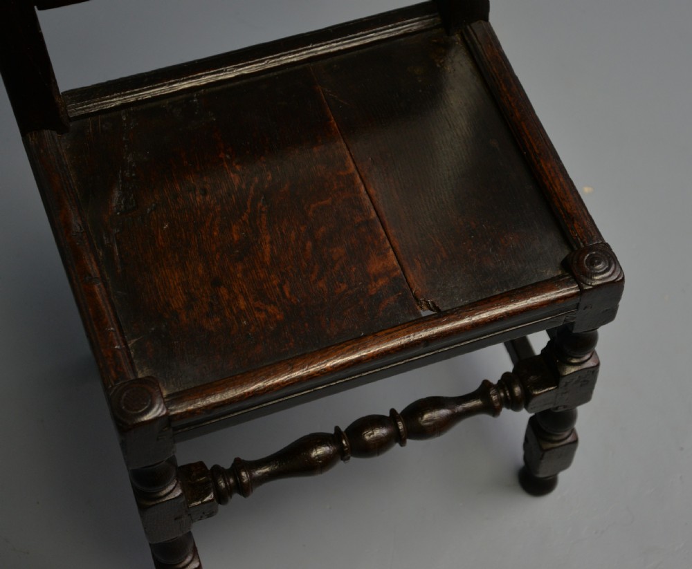 A dark carved oak 17th-century style backstool chair featuring an arched carved cresting rail, a carved floral back panel, turned front legs, and stretchers. View XIX