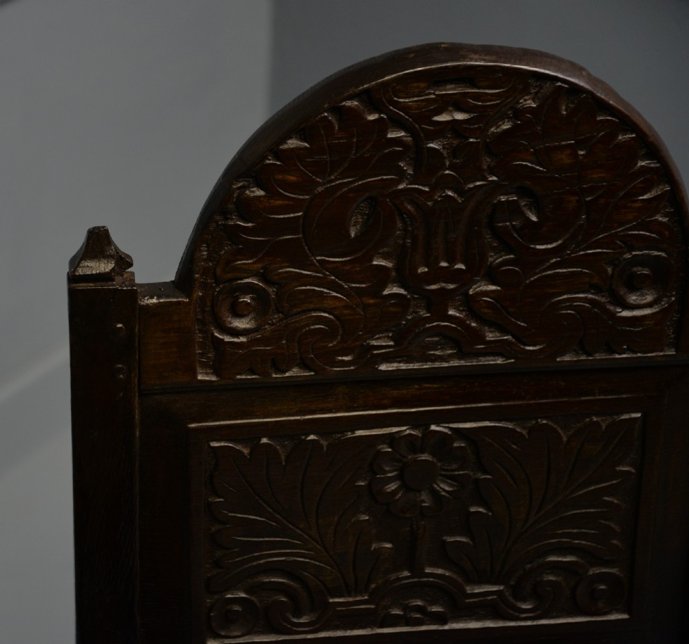 A dark carved oak 17th-century style backstool chair featuring an arched carved cresting rail, a carved floral back panel, turned front legs, and stretchers. View XX