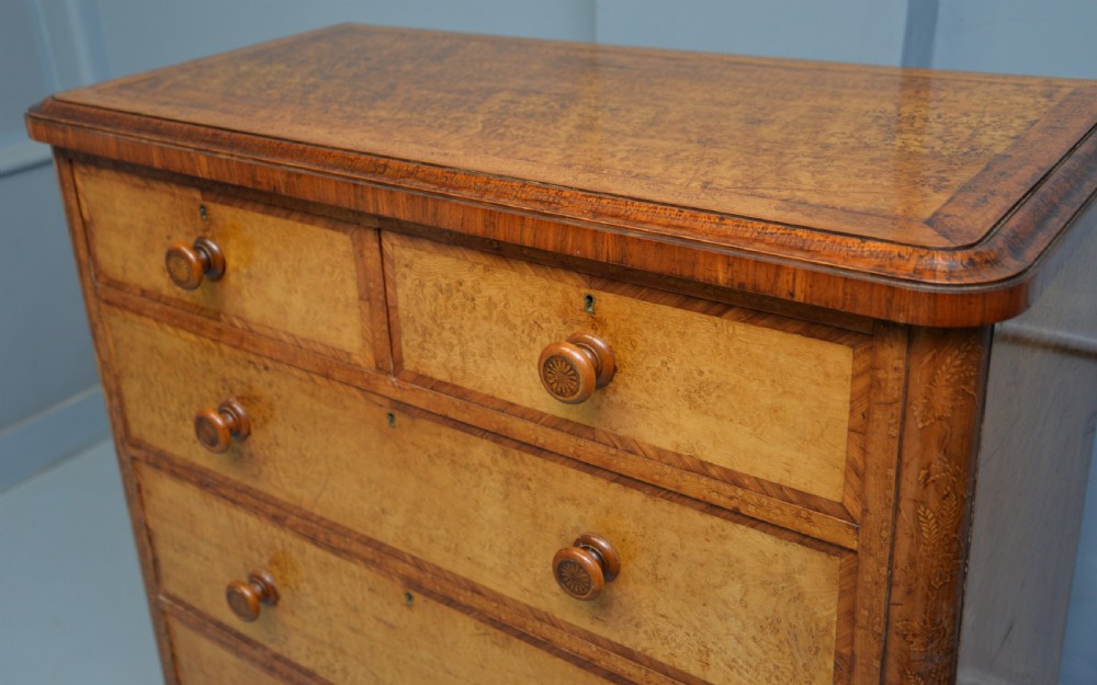 A Victorian satinwood chest of drawers featuring two small upper drawers above three full-width drawers with turned rosette knobs and a plinth base. View XVII