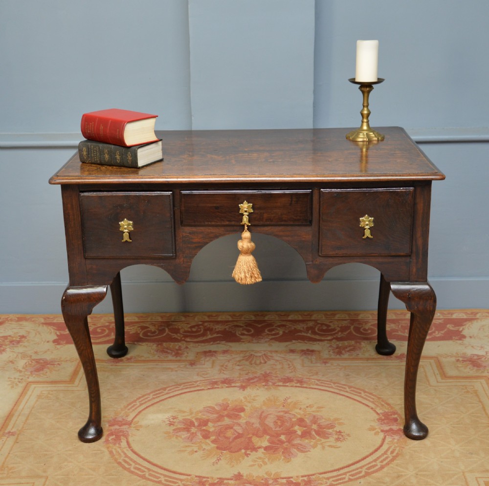 An early 18th-century George I dark oak lowboy featuring three drawers with brass handles, a shaped kneehole apron, and cabriole legs ending in pad feet. View II