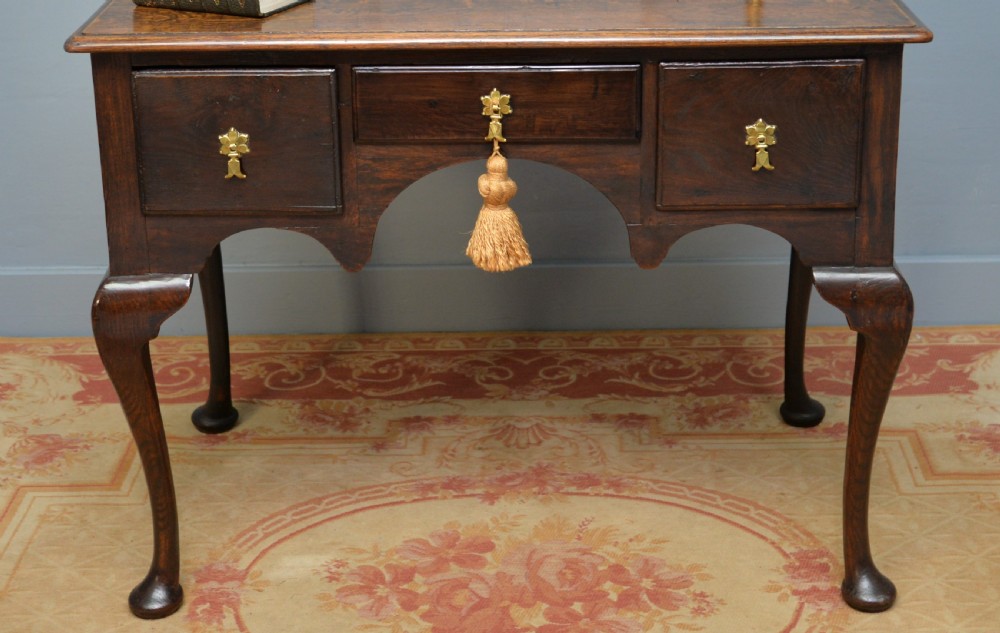 An early 18th-century George I dark oak lowboy featuring three drawers with brass handles, a shaped kneehole apron, and cabriole legs ending in pad feet. View V