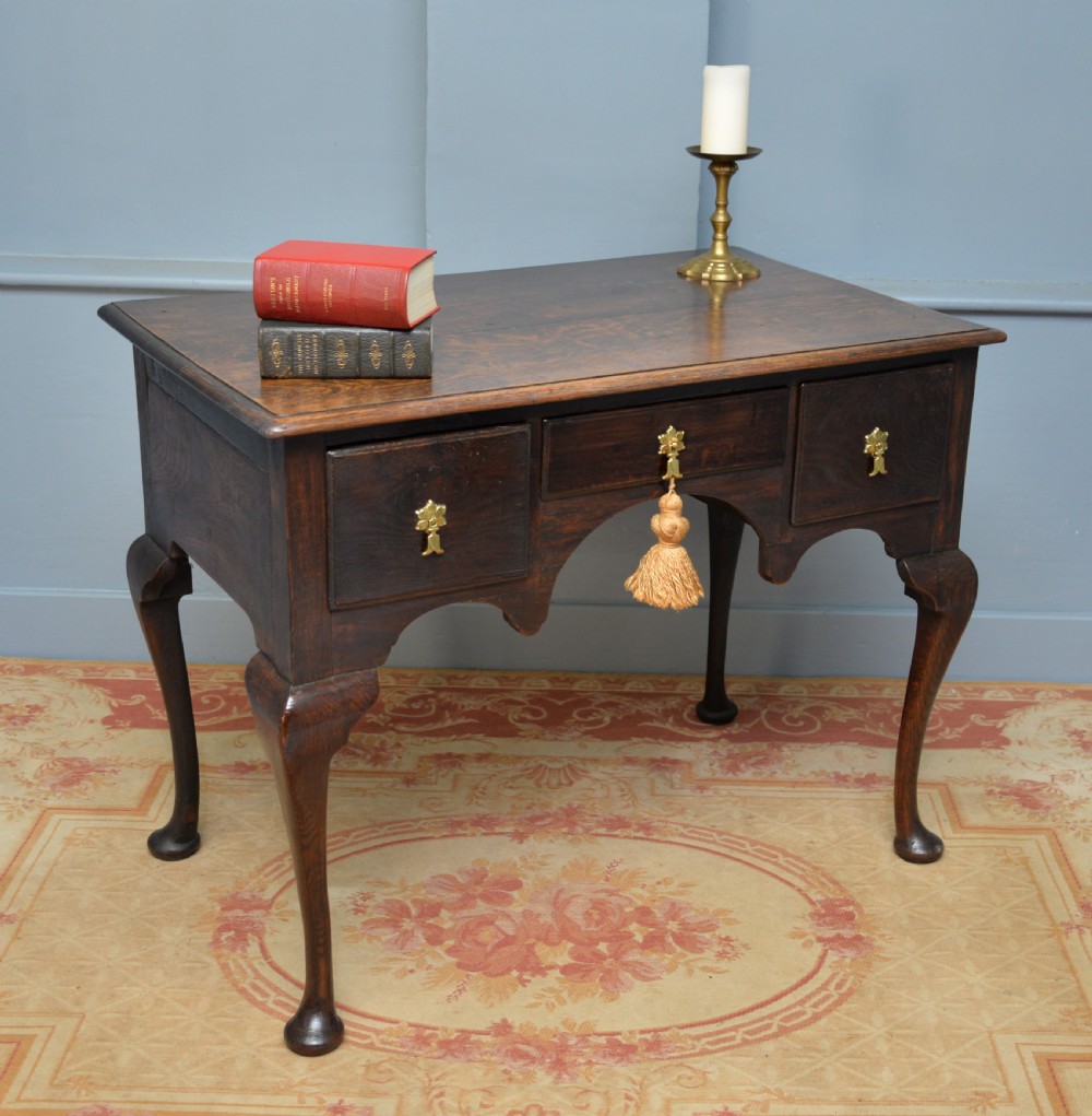 An early 18th-century George I dark oak lowboy featuring three drawers with brass handles, a shaped kneehole apron, and cabriole legs ending in pad feet. View VII