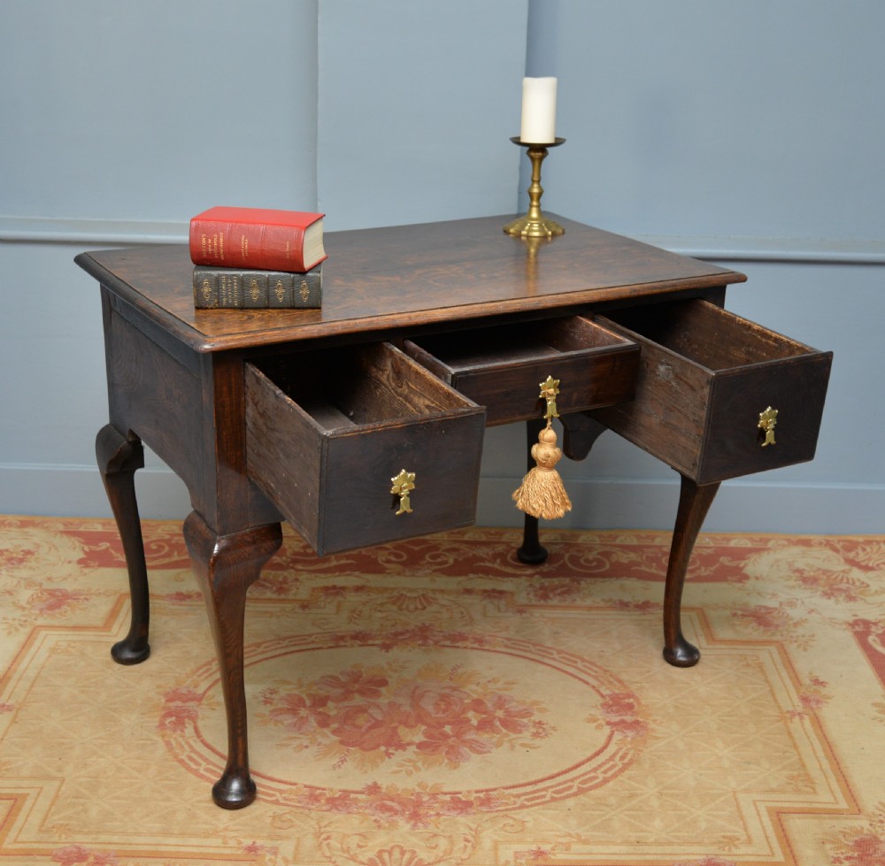 An early 18th-century George I dark oak lowboy featuring three drawers with brass handles, a shaped kneehole apron, and cabriole legs ending in pad feet. View VIII