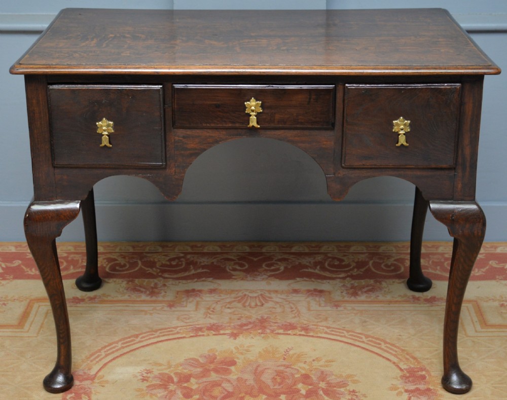 An early 18th-century George I dark oak lowboy featuring three drawers with brass handles, a shaped kneehole apron, and cabriole legs ending in pad feet. View X